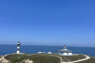 A white lighthouse and keeper’s house on a green headland above a deep blue sea