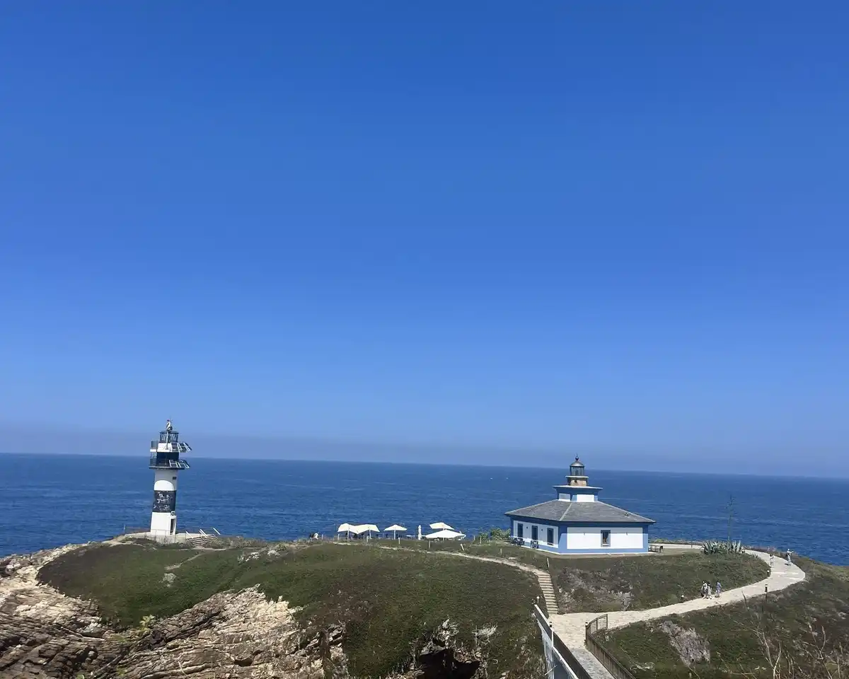 A white lighthouse and keeper’s house on a green headland above a deep blue sea