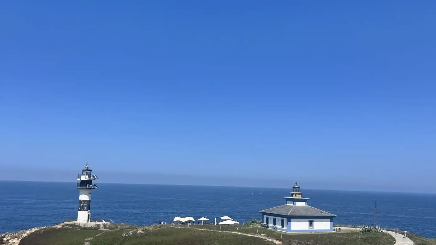 A white lighthouse and keeper’s house on a green headland above a deep blue sea