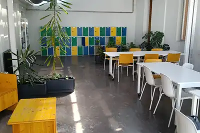 A bright shared workspace with white tables, yellow benches, potted plants and a wall of coloured lockers