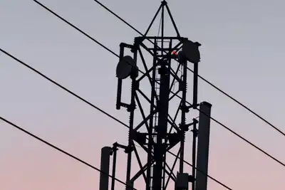 A steel radio mast with antennas and cables, silhouetted against a pink and blue evening sky