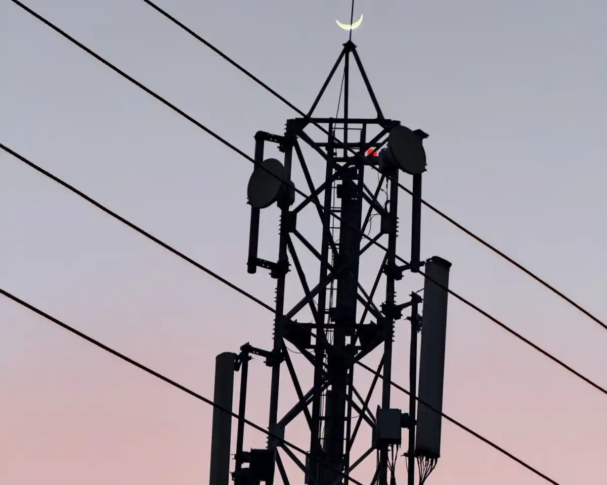 A steel radio mast with antennas and cables, silhouetted against a pink and blue evening sky