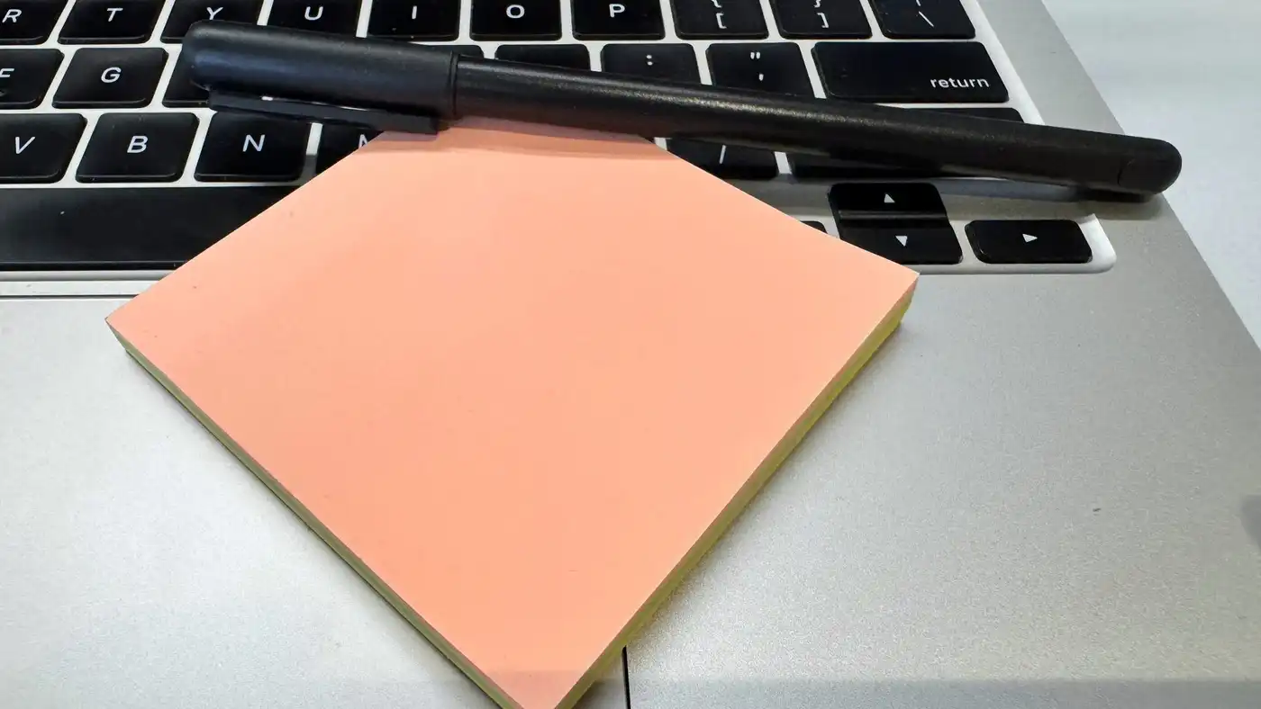 A pad of peach sticky notes and a black pen resting on a laptop keyboard