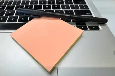 A pad of peach sticky notes and a black pen resting on a laptop keyboard