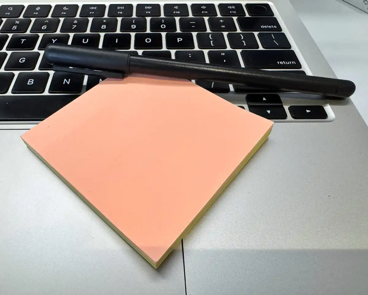 A pad of peach sticky notes and a black pen resting on a laptop keyboard